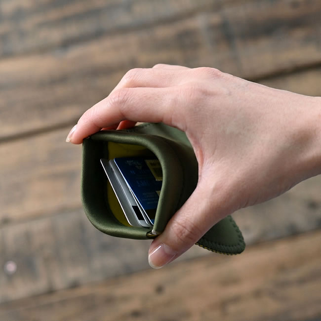 手で両端を押して開いたオリーブ色のコイン＆カードホルダー