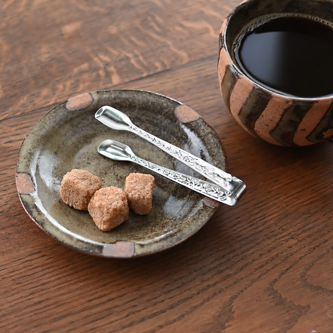 角砂糖の小皿に置いたステンレス シュガートングとコーヒーカップ